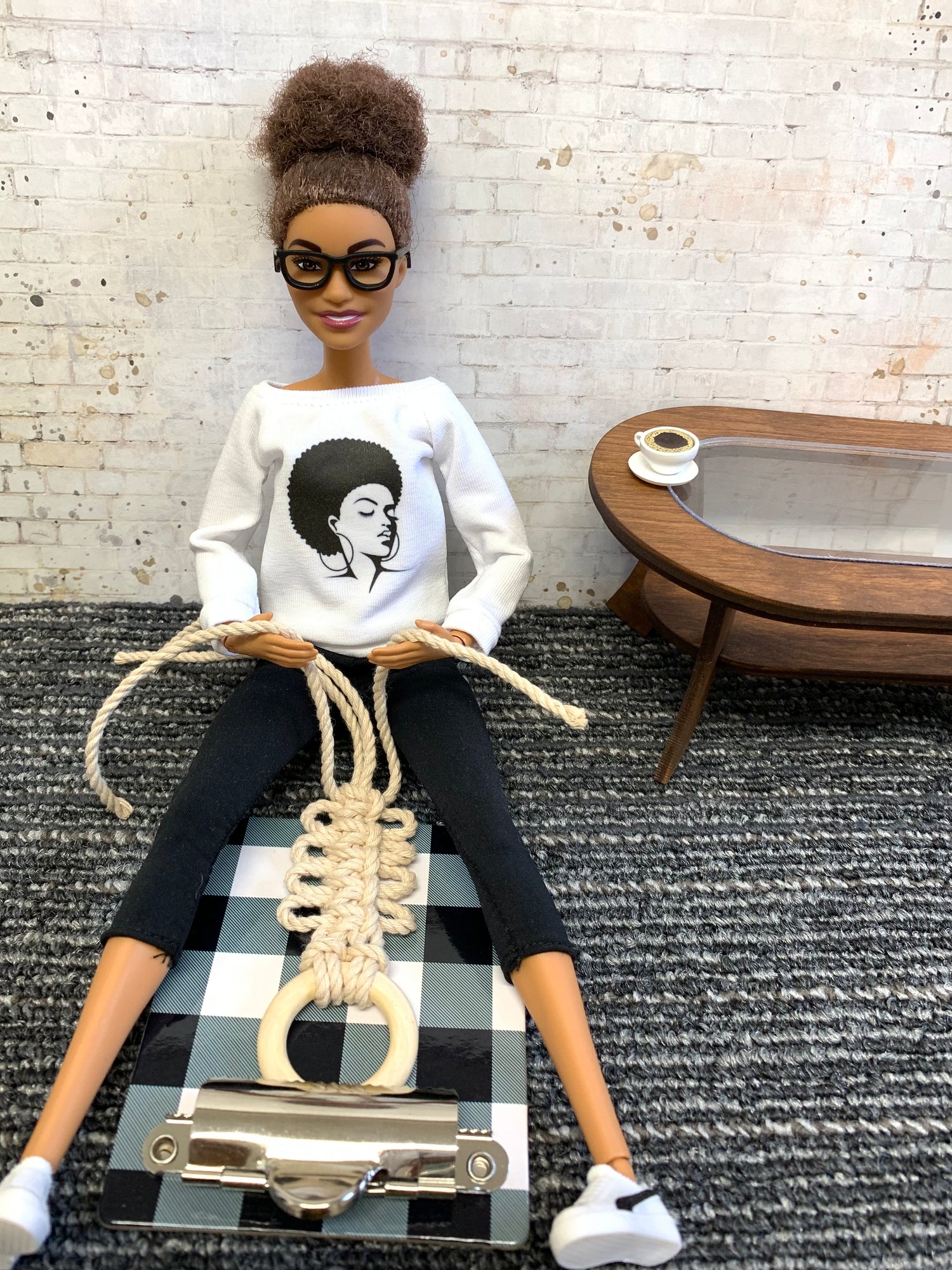 Barbie doll sitting on a carpeted floor working on macrame knots.